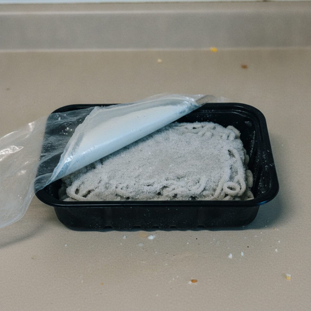 A frozen ready meal in a black plastic tray with the film half peeled back